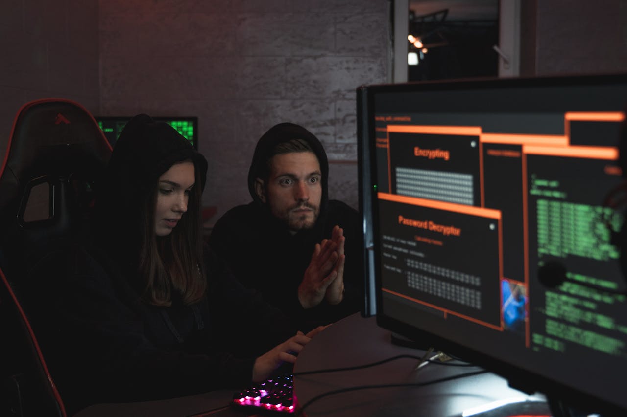Services Cybersecurity experts in hoodies analyzing encrypted data on computer screens in an indoor setting.